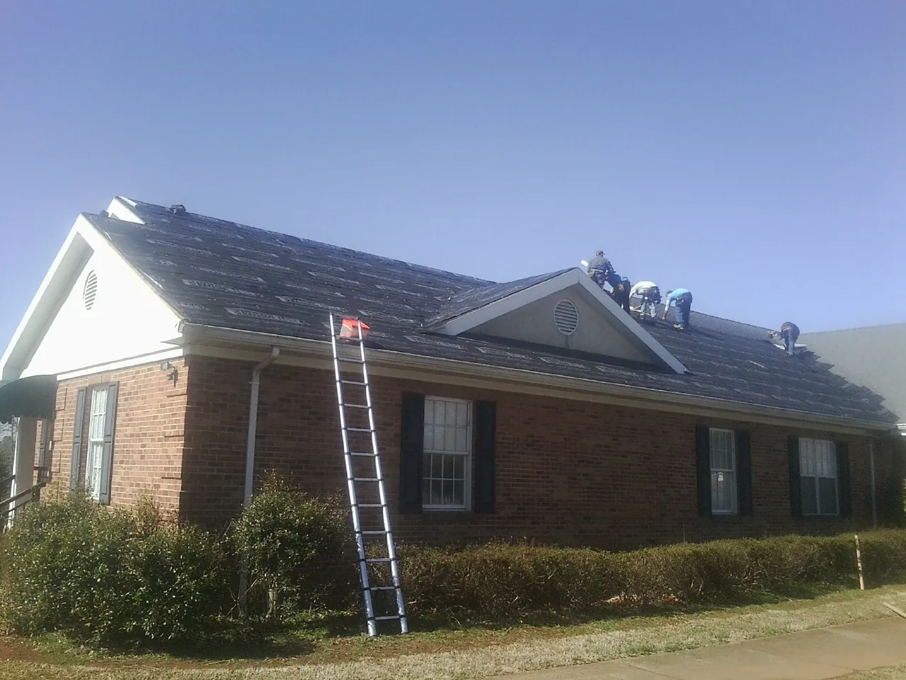 Crew tearing shingles off a brick ranch roof with a ladder set — Metal Roof Repair work by our crew in Norris